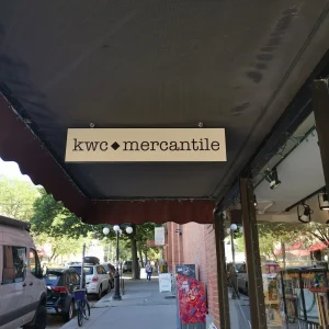 a hanging blade sign underneath an awning outside a store